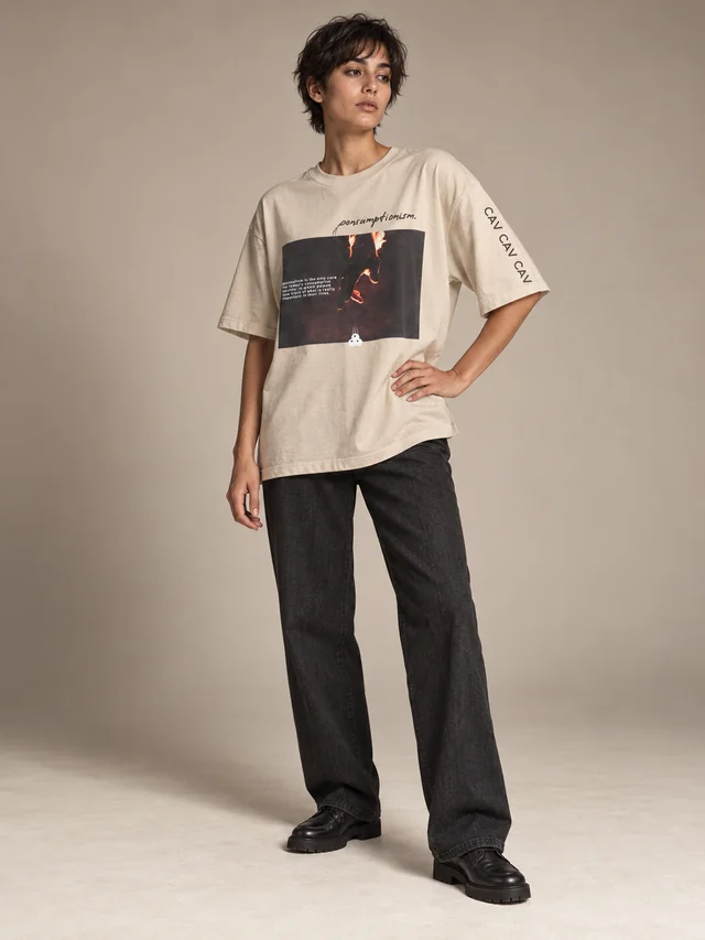 Full-body studio exploration: a new short-haired model wearing the consumptionism graphic on an oversized beige T-shirt